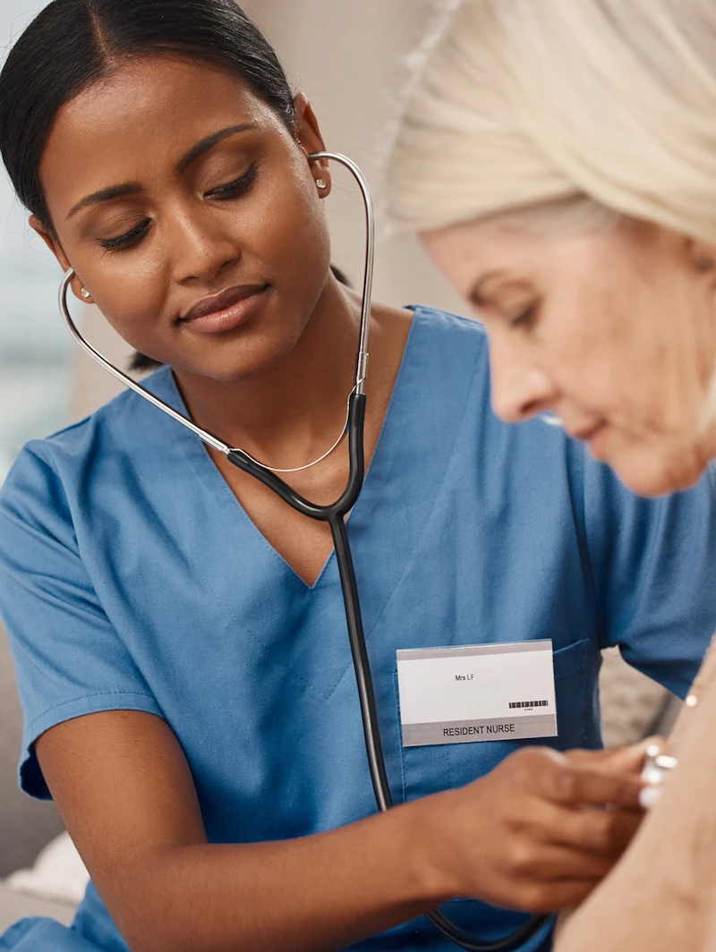 Healthcare worker using a stethoscope on a patient, representing in-home care and communication support